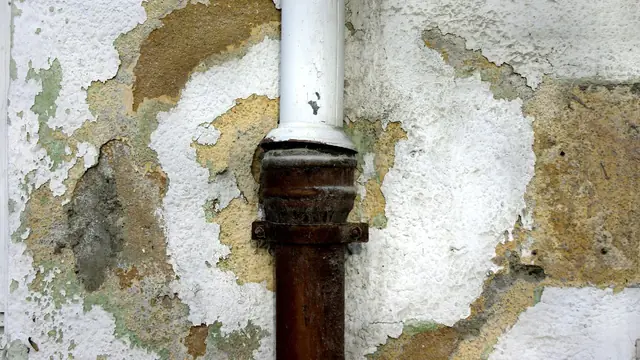 Peeling, water-stained plaster around a corroded pipe on a wall